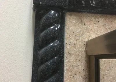 Close-up of a black, textured picture frame corner against a light wall and beige background.