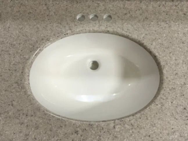 Oval white sink countertop with faucet hole and beige speckled surface