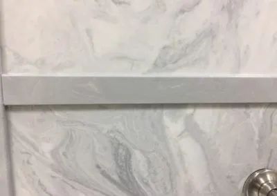 White marble-tile wall with a horizontal trim and a chrome fixture in the lower right.