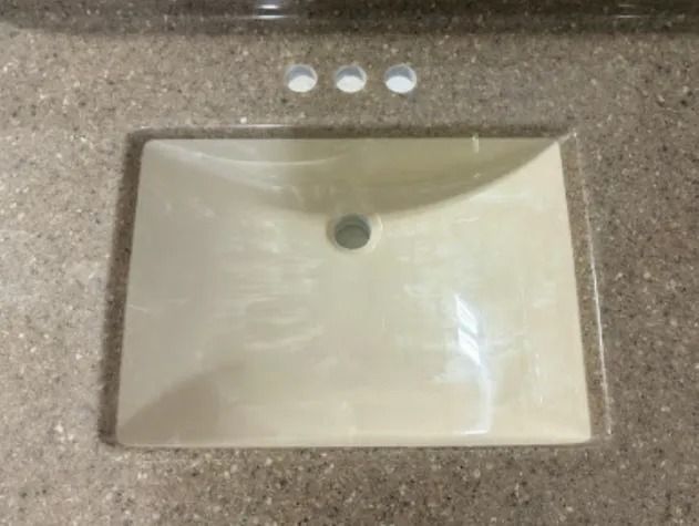 Beige bathroom sink set in a speckled countertop with three silver faucet knobs above it