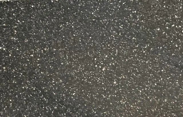 Dark speckled textured surface with scattered white specks, like asphalt or stone.
