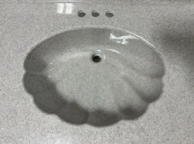 White scalloped sink basin with a drain hole on a gray countertop.