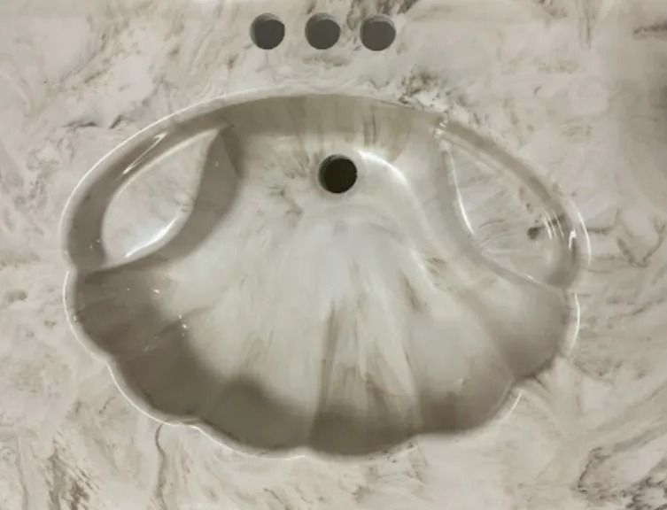 Oval white bathroom sink with three faucet holes on a marble countertop