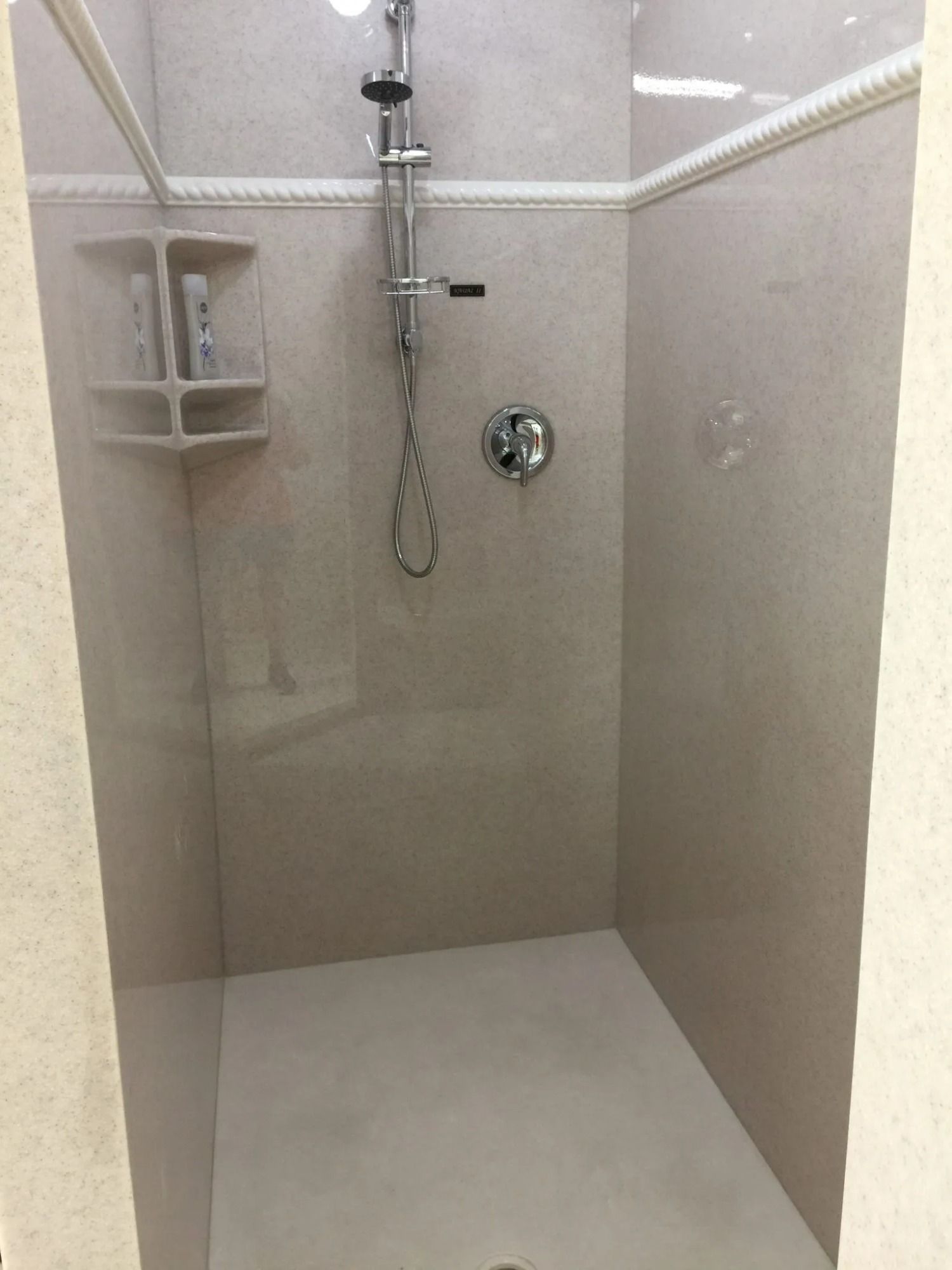 Empty beige tiled shower with handheld showerhead and built-in corner shelf.