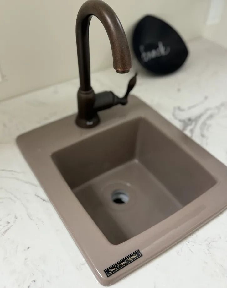 Modern kitchen sink with bronze faucet and beige basin on white marble countertop
