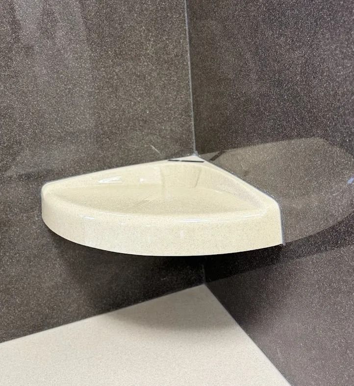 White triangular corner shelf mounted on a dark tiled wall above a tiled floor.