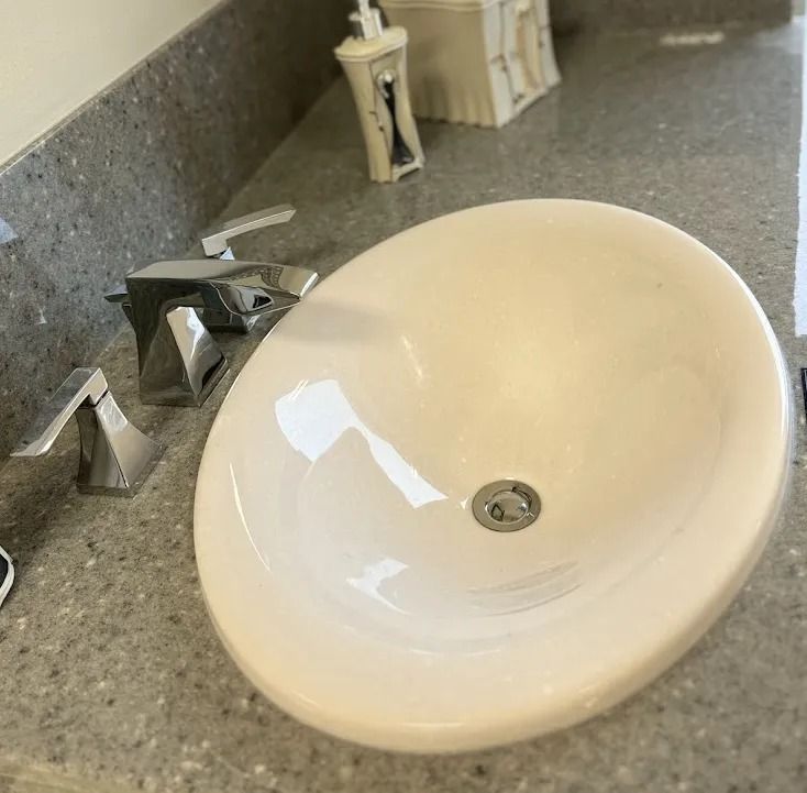 White bathroom sink with chrome faucet on a speckled countertop, viewed at an angle.