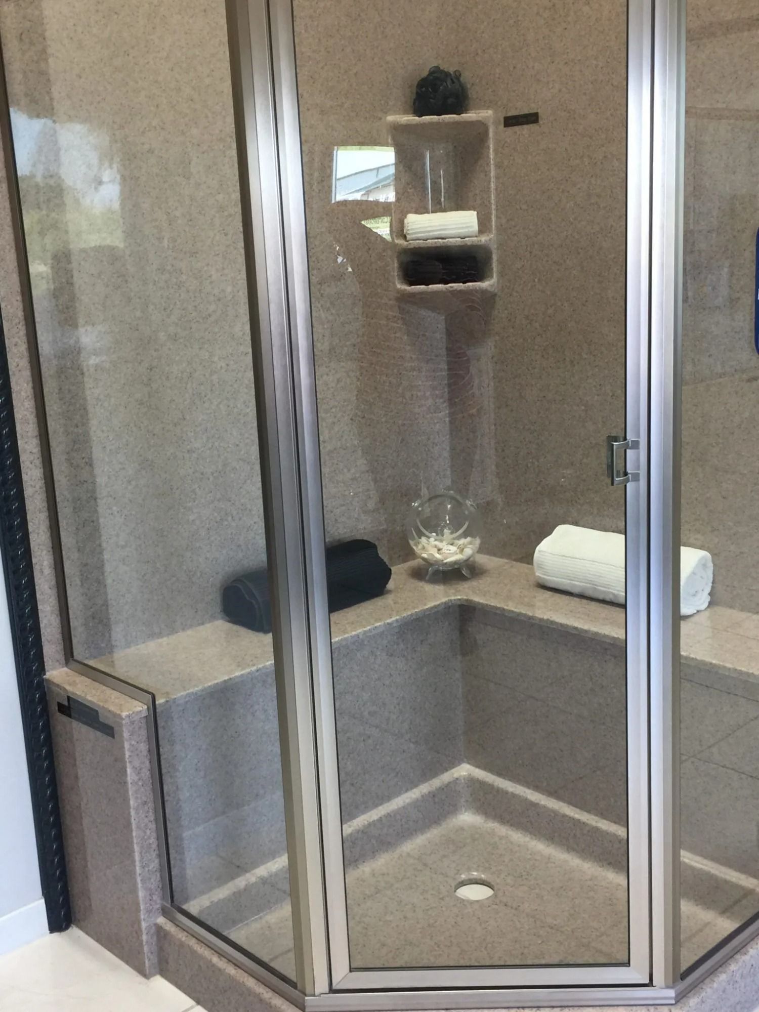 Glass corner shower with gray tile, built-in shelf, and folded white towels on the ledge