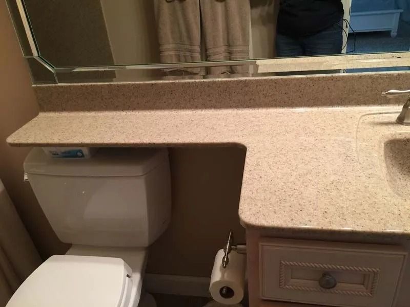 Bathroom vanity with tan countertop, mirror, sink, and toilet below the counter cutout