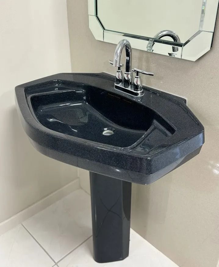 Black pedestal sink with chrome faucet and mirror in a restroom corner