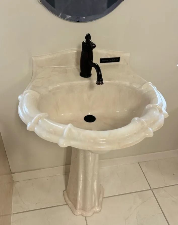 White pedestal sink with black faucet in a tiled restroom.