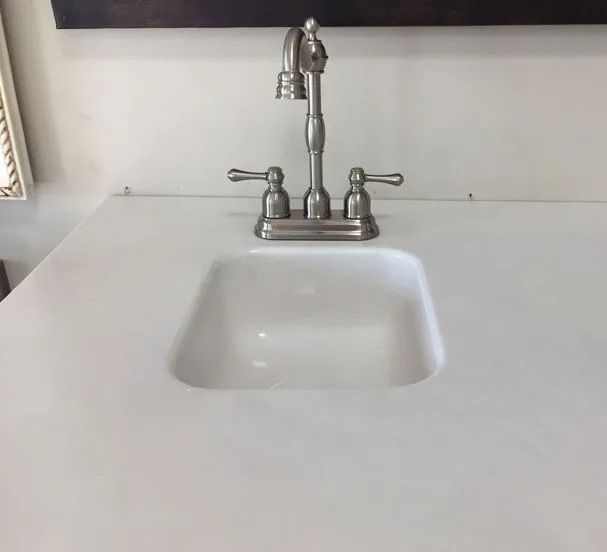 White bathroom sink with chrome faucet on a white countertop against a plain wall