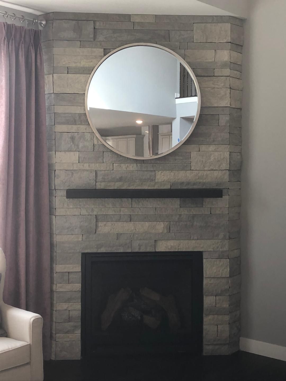 A fireplace with a round mirror above it