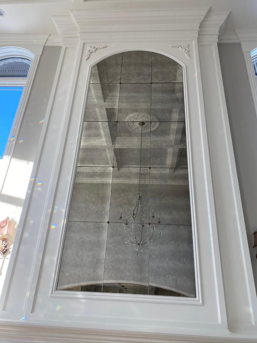 A room with a large vertical mirror on it and a chandelier hanging from the ceiling