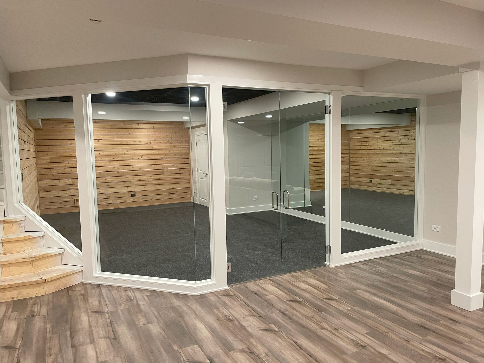 A basement with hardwood floors, stairs, and a room with glass walls