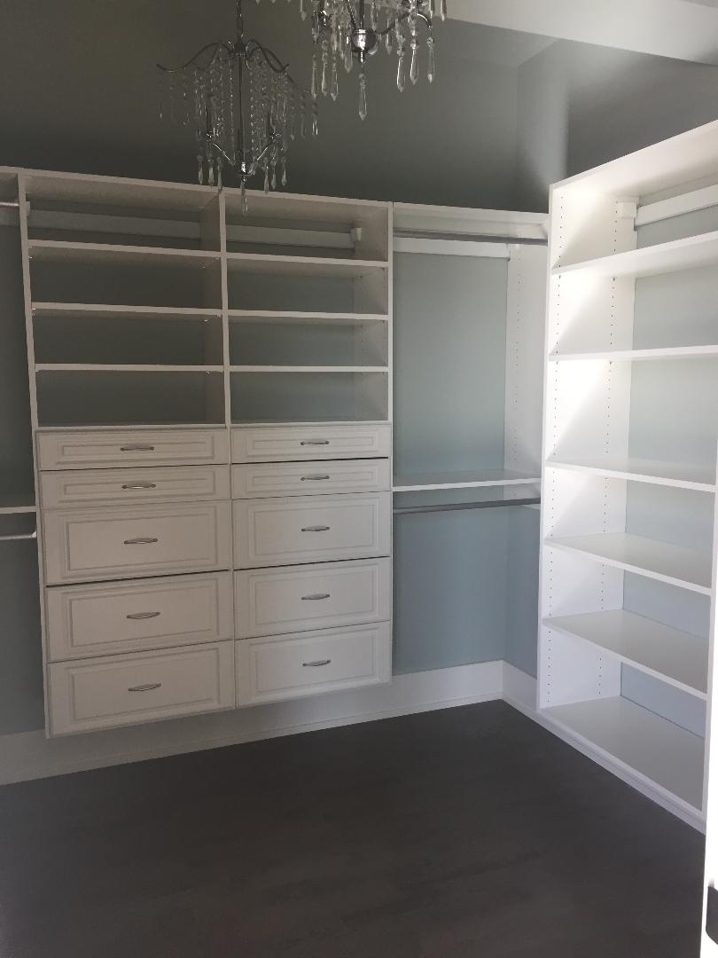 A walk in closet with lots of shelves and drawers and a chandelier hanging from the ceiling.