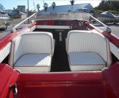 The inside of a red boat with white seats and a steering wheel.