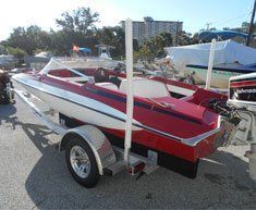 A red and white boat is on a trailer in a parking lot.