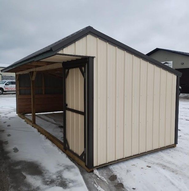 Cream-colored shed with a dark roof and door, attached to a wooden porch with a mesh screen, on a snowy ground.