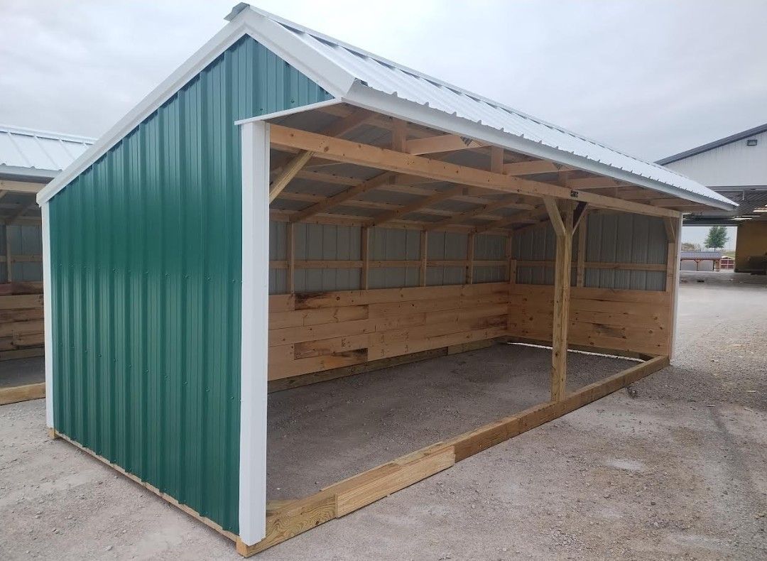 Green and white metal shed with wooden frame and gravel floor.