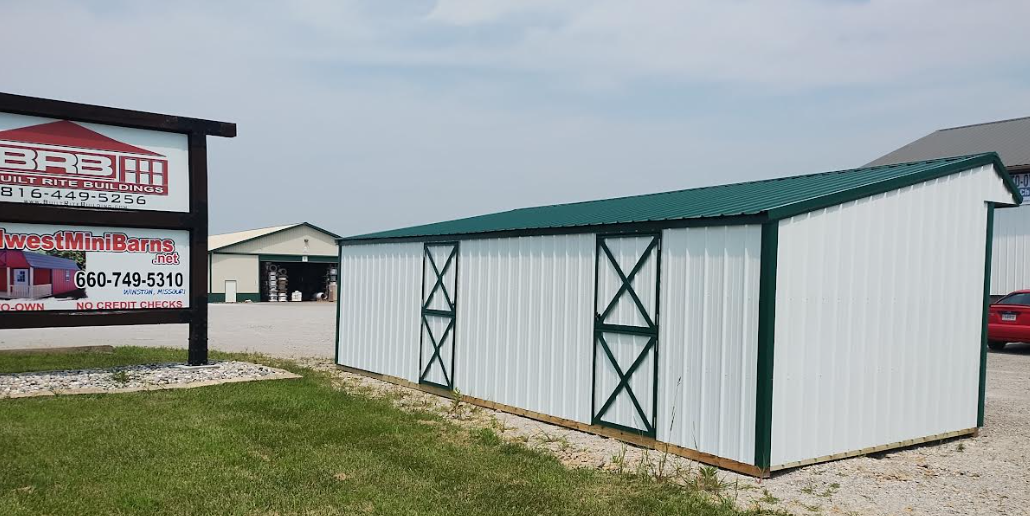 White metal building with green trim and sign in front of building.
