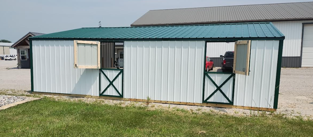 White barn with green roof and trim, two stalls with open doors and windows, sitting on green grass.