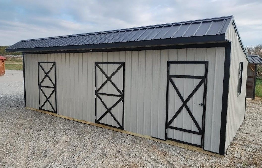 Gray shed with black trim and doors, metal roof, on gravel.