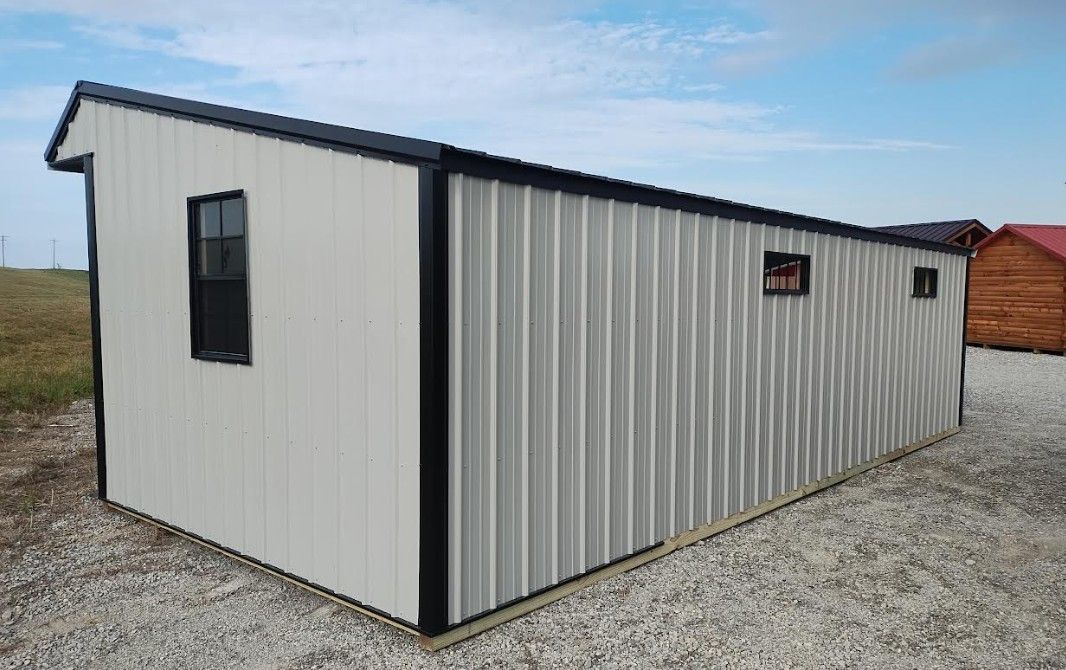 Long, light gray metal shed with black trim and a black roof. Three small windows are visible.