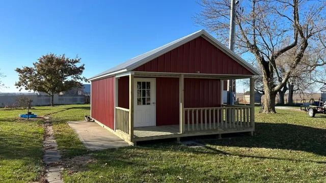 A small red shed with a porch in the middle of a grassy field.