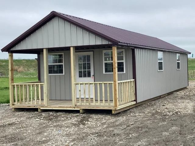 A small house with a porch and a purple roof is sitting on top of a dirt field.