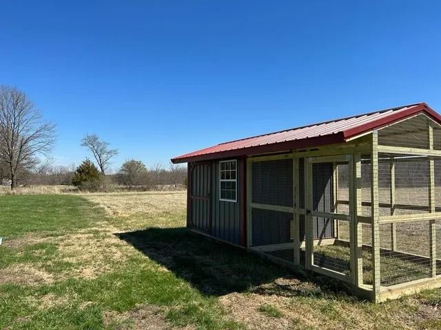 A chicken coop is sitting in the middle of a grassy field.