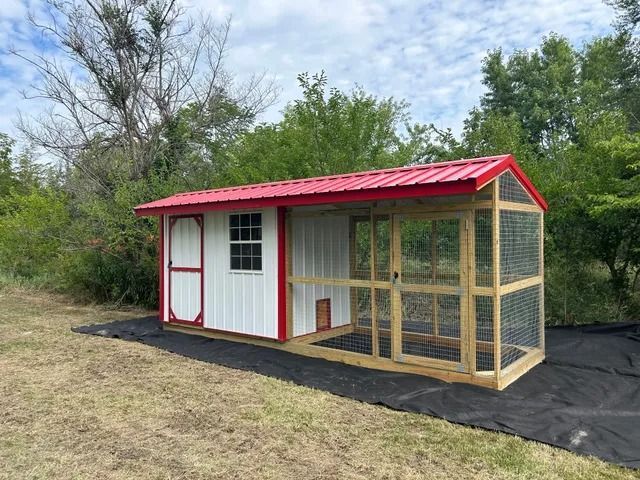 A chicken coop with a red roof is sitting in the middle of a field.