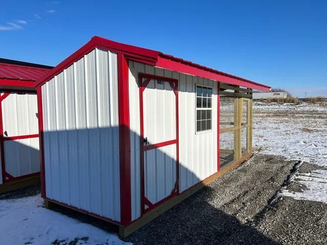 A white shed with a red roof is in the middle of a snowy field.