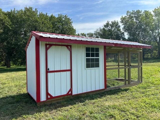 A white shed with a red trim is sitting in the middle of a grassy field.