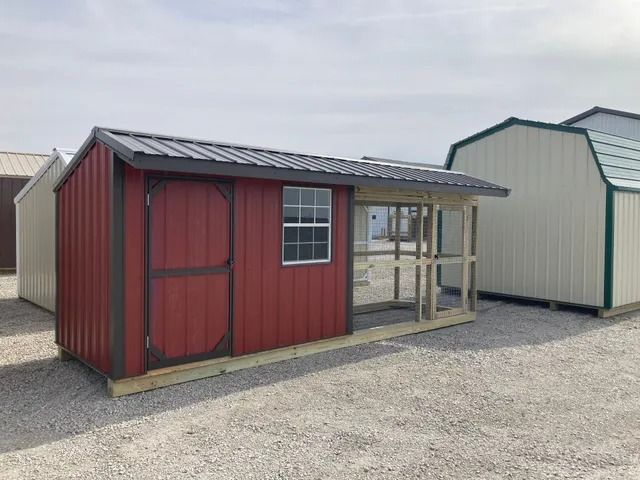 A red shed with a black roof is sitting in a gravel lot.