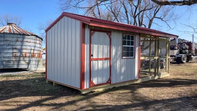 A small white shed with a red roof is sitting in the middle of a field.