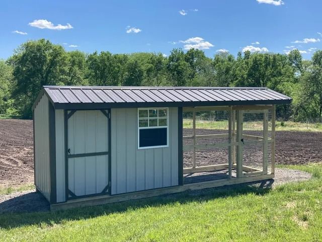 A small shed with a chicken coop attached to it is sitting in the middle of a grassy field.