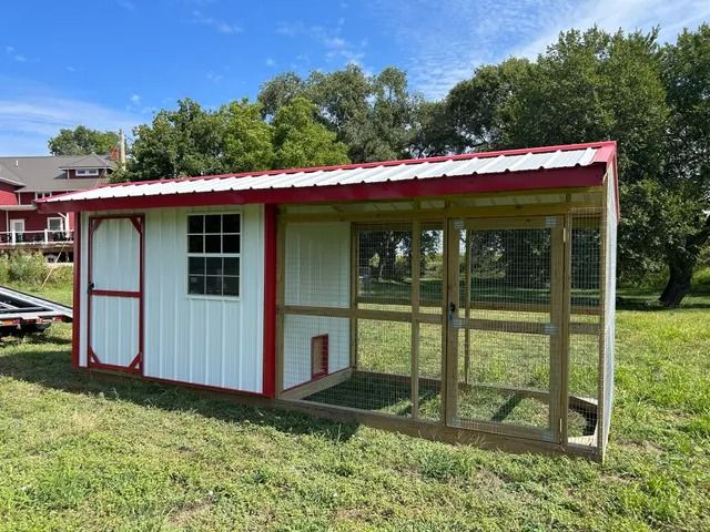 A white and red chicken coop is sitting in the middle of a grassy field.