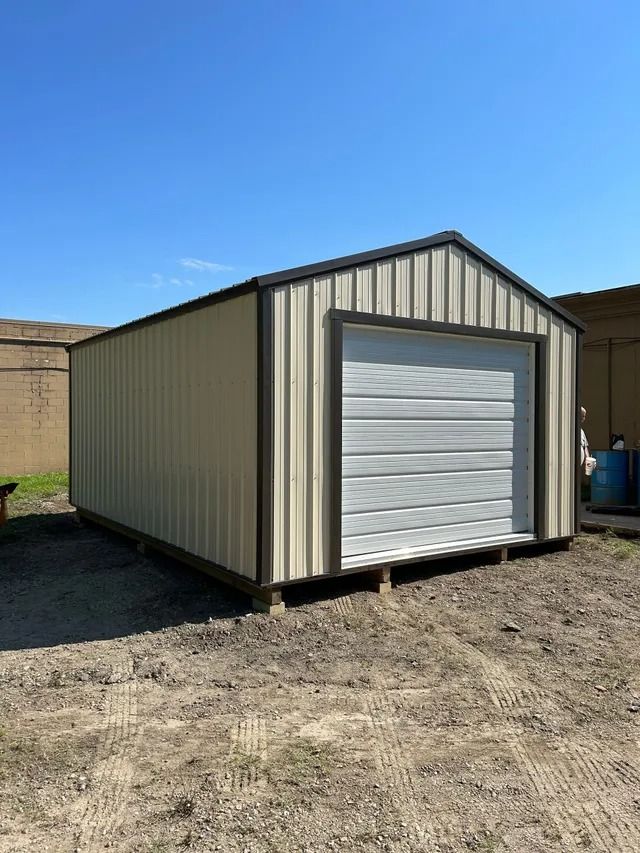 A metal garage with a white garage door is sitting in the middle of a dirt field.