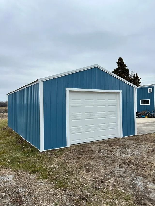 A blue garage with a white door is sitting in the middle of a dirt field.