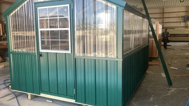 A green shed with a door and window is sitting in a building.