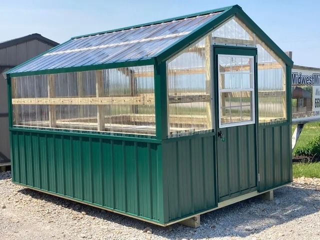 A greenhouse with a clear glass roof is sitting on a gravel road.