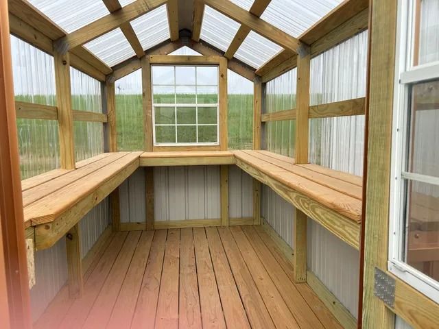 The inside of a greenhouse with wooden shelves and a window.