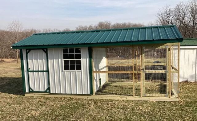 A white shed with a green roof and a chicken coop attached to it.
