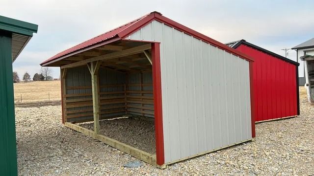 A red and white shed with a red roof is sitting on top of a gravel lot.