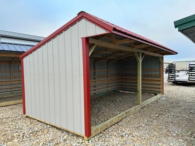 A white shed with a red roof is sitting on top of a gravel lot.
