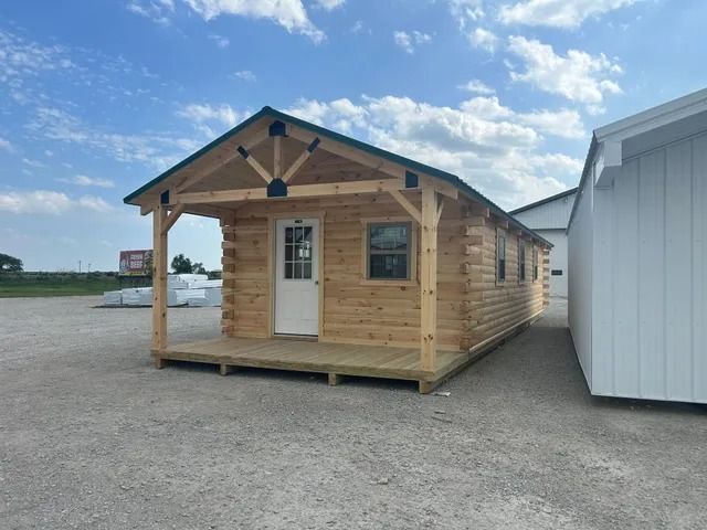 A small log cabin with a porch and a green roof