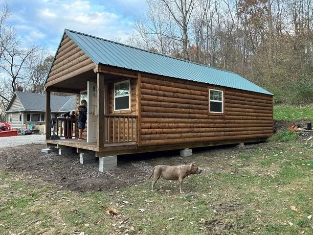 A dog is standing in front of a log cabin.