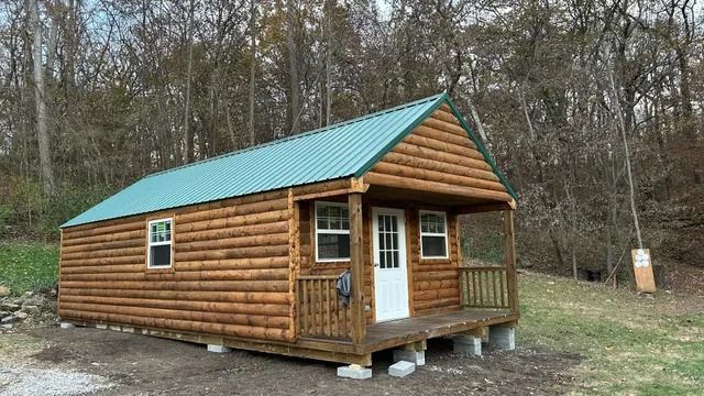 A small log cabin with a green roof and a porch.