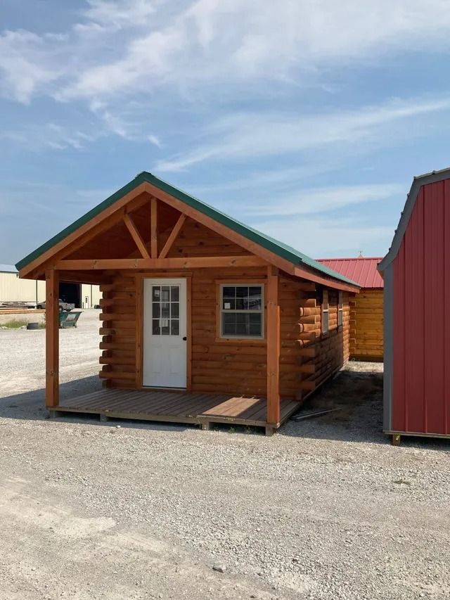 A small log cabin with a porch and a green roof